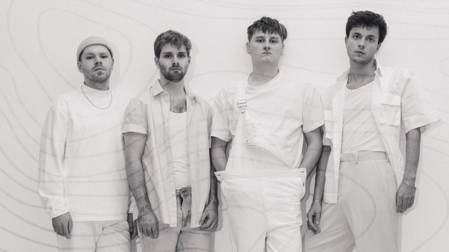 Ein Schwarz Weiß Bild der vierköpfigen Band Razz. Sie stehen nebeneinander an einer Wand und schauen direkt in die Kamera. Alle tragen weiße Kleidung