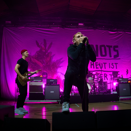 Die Donots auf der Bühne vor ihrem pink angestrahlten Banner